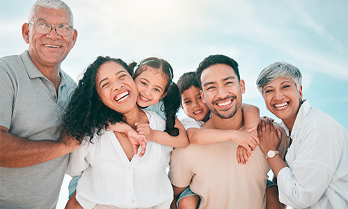 A multi-generational family smiling at the camera, standing outside in the sunshine