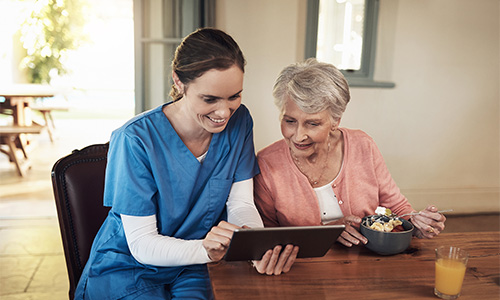 An in-home nurse looks at a tablet with an elder woman