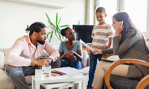 A family sits around the couch as they discuss some paperwork