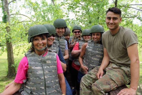 A diverse group of people in military gear smile happily at the camera.