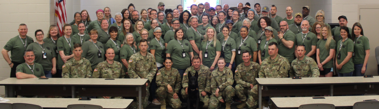 A large classroom is filled with a crowd of arranged participants in military colors.
