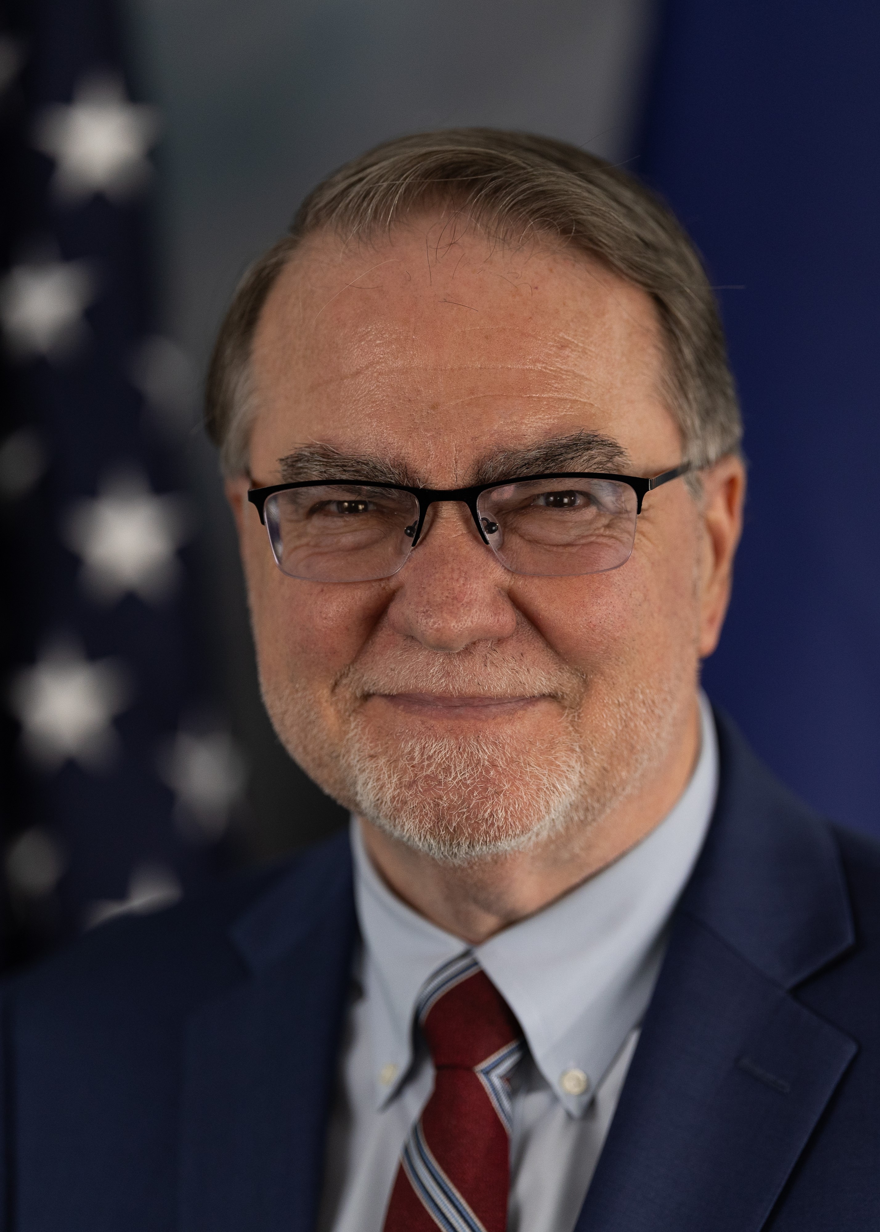 Headshot of Commissioner Langefeld infront of  a flag